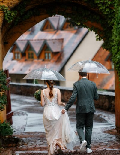 Hand in Hand unter Regenschirmen spaziert das Brautpaar durch verwinkelte Altstadtgassen – festgehalten von Helene Karsten Hochzeitsfotografie.