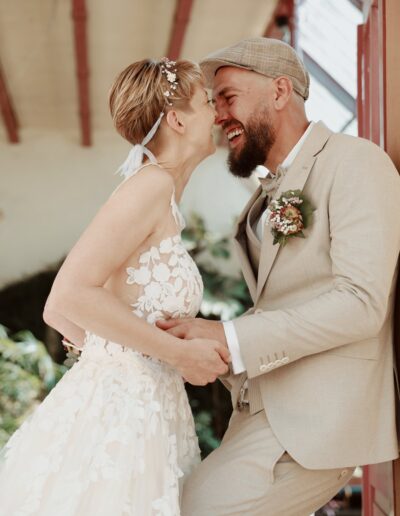 Ein verliebtes Hochzeitspaar steht nah beieinander, lacht sich herzlich an und hält sich zärtlich an den Händen – eine romantische Hochzeitsaufnahme voller Freude.