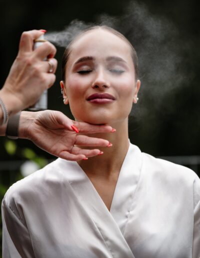 Die Brautjungfer mit geschlossenen Augen genießt das Fixierspray – Nahaufnahme beim Styling vor der Hochzeit.