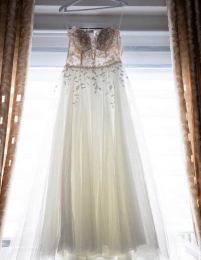 Ein Brautkleid hängt auf einem Bügel in der Mitte des Fensters, links und rechts sieht man noch die Vorhänge.