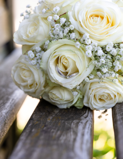 Detailaufnahme von einem Brautstrauss mit weissen Rosen, in einer befinden sich 2 silberne Eheringe.
