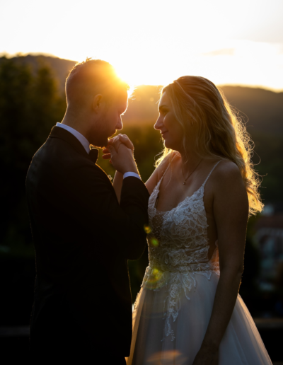 Sonnenuntergang, der Bräutigam gibt der Braut einen Handkuss und schaut ihr dabei in die Augen. Ihre offenen Haare sind vom Licht umrahmt.