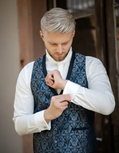 Der Bräutigam richtet sich gerade für die Hochzeit und macht gerade seine Manschetten Knöpfe zu. Ein Arm ist gebeugt und Blick geht zum Handgelenk.