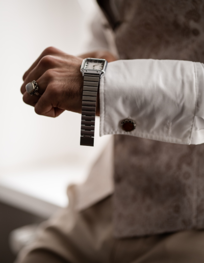 Eine männliche Hand zieht eine silberne Armbanduhr an, auf dem Ringfinger steckt ein großer Ring.