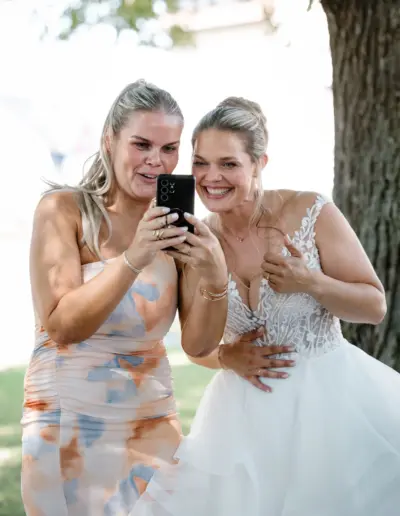 Braut und Gast schauen sich ein Bild auf dem Handy an und sind beide erstaunt und voller Freude darüber.