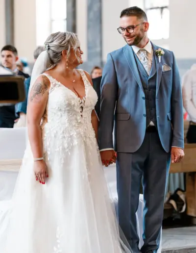 Brautpaar steht vor dem Altar, heben sich an de Händen und schauen sich glücklich an.