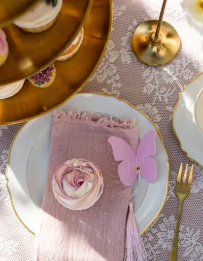 Ein dekorierter Tisch zu Kaffee aufgebaut, Ansicht von oben. Auf dem Teller liegt ein Cupcake. Weitere Cupcakes sind auf einer Etagere am Rande sichtbar. eine leere Tasse steht daneben.