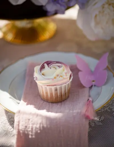 Detailaufnahme von einem cupcake auf einem Teller liegend, neben ihm ist ein rosafarbener Schmetterling aus Papier als Platzzuweisung.