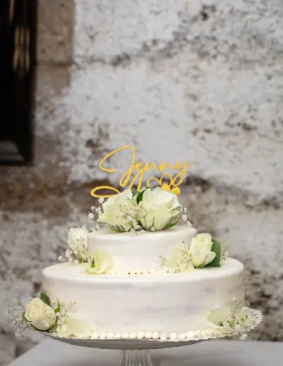 Eine Hochzeitstorte dekoriert mit weisen Rosen und den Namen des Brautpaares.