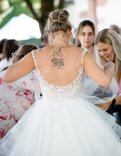 Gäste bestaunen das Kleid der Braut, die Braut ist von hinten zu sehen und ein Tattoo einer Tänzerin befindet sich auf ihrem Rücken.